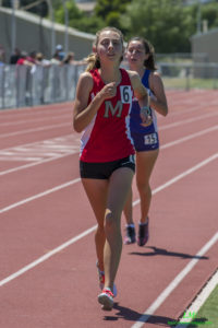 Athlete prepares for pole vault on a track with others watching.