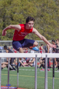 Athlete mid-air jumping over a hurdle during a track event.