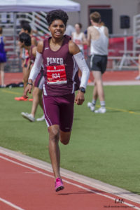Athlete prepares for pole vault on a track with others watching.