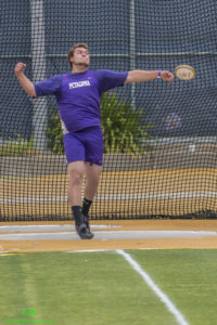 Athlete prepares for pole vault on a track with others watching.