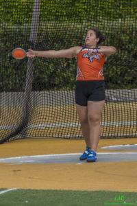 Athlete prepares for pole vault on a track with others watching.