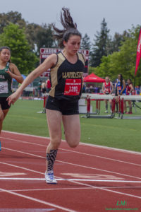 Athlete prepares for pole vault on a track with others watching.