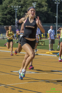 Athlete prepares for pole vault on a track with others watching.