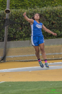 Athlete prepares for pole vault on a track with others watching.
