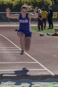 Athlete mid-air during a long jump event on a track.