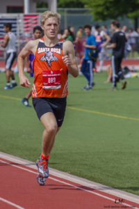 Athlete prepares for pole vault on a track with others watching.