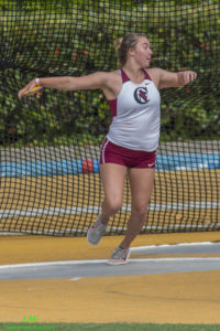 Athlete prepares for pole vault on a track with others watching.