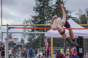 Athlete mid-air during a pole vault attempt at an outdoor event.