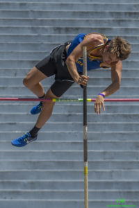 Athlete prepares for pole vault on a track with others watching.