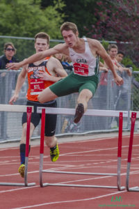 Athlete prepares for pole vault on a track with others watching.