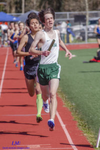 Two male athletes racing on a track during a relay event.