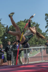 Athlete prepares for pole vault on a track with others watching.