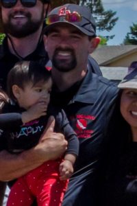 Man holding a child with a woman smiling beside them outdoors.