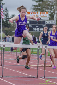 Athletes clearing hurdles during a track race outdoors.