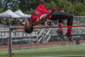 Athlete prepares for pole vault on a track with others watching.