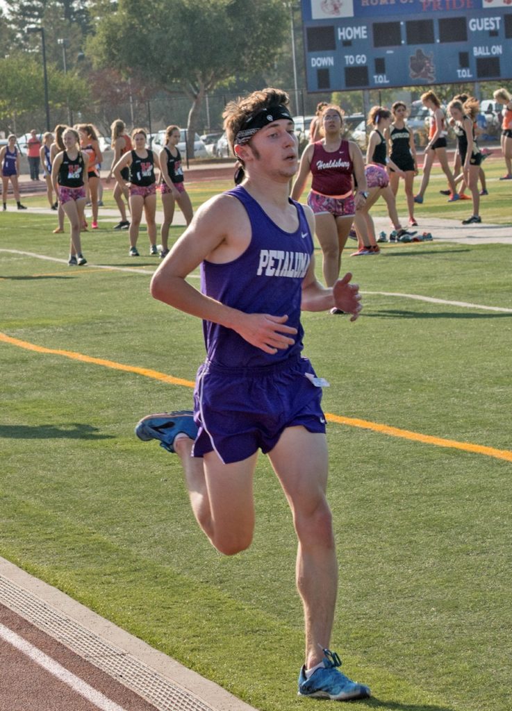 Athlete prepares for pole vault on a track with others watching.