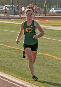 Athlete prepares for pole vault on a track with others watching.