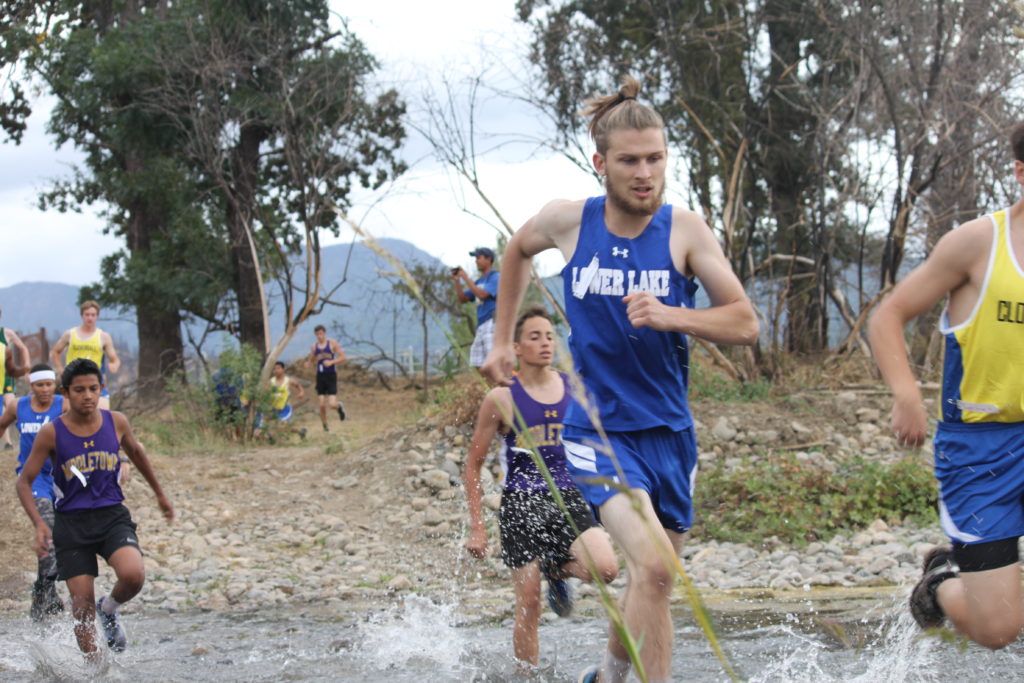 Athlete prepares for pole vault on a track with others watching.