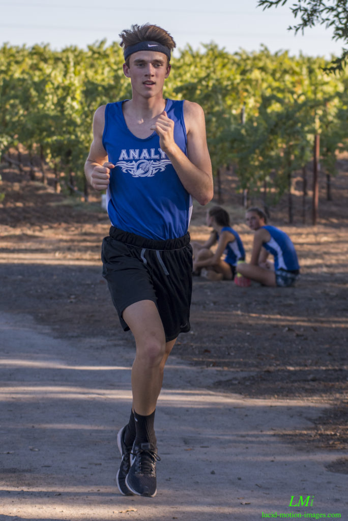 Athlete prepares for pole vault on a track with others watching.