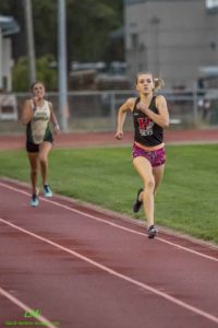 Athlete prepares for pole vault on a track with others watching.