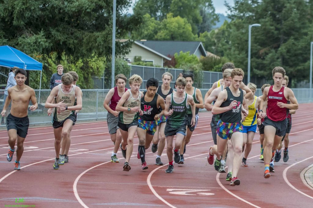Athlete prepares for pole vault on a track with others watching.