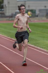 Athlete prepares for pole vault on a track with others watching.