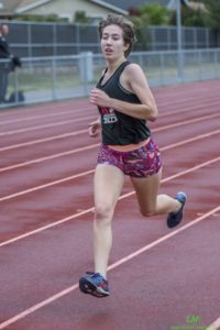 Athlete prepares for pole vault on a track with others watching.