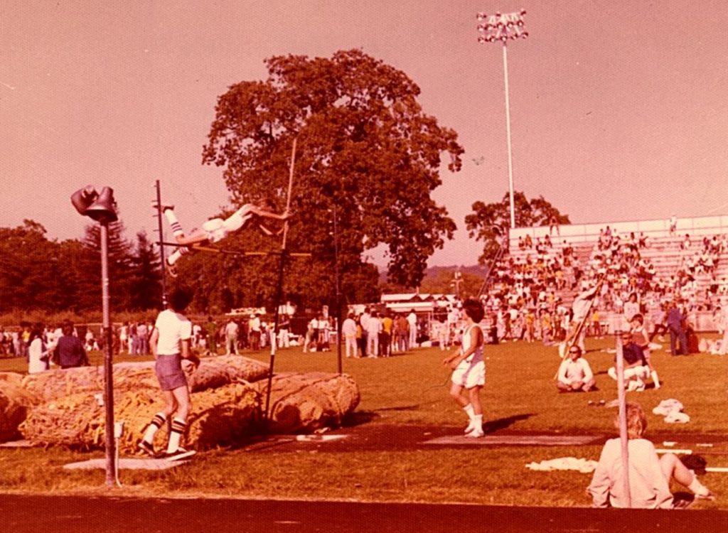 Athlete prepares for pole vault on a track with others watching.