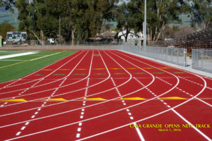 Athlete prepares for pole vault on a track with others watching.