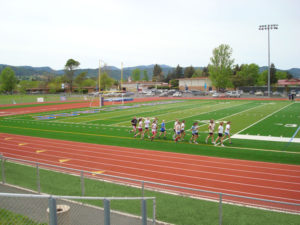 Athlete prepares for pole vault on a track with others watching.