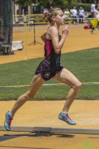 Athlete prepares for pole vault on a track with others watching.