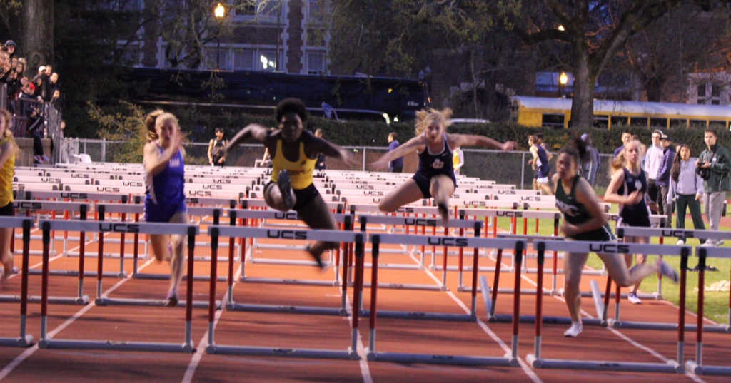 Athlete prepares for pole vault on a track with others watching.