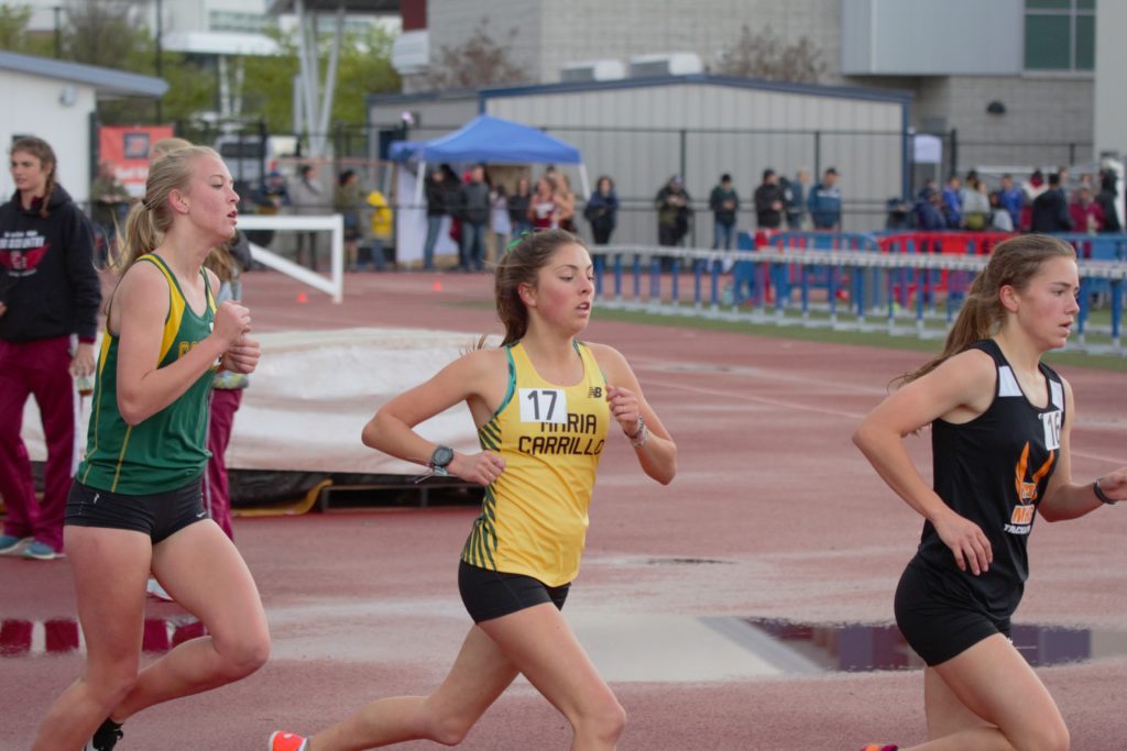 Athlete prepares for pole vault on a track with others watching.