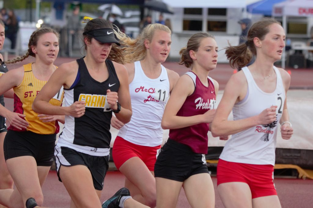 Athlete prepares for pole vault on a track with others watching.