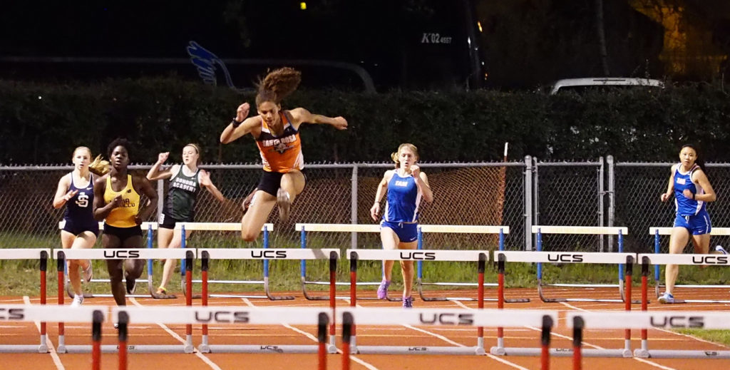 Athlete prepares for pole vault on a track with others watching.
