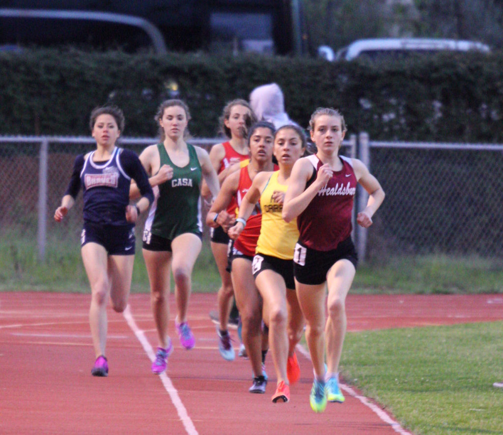 Athlete prepares for pole vault on a track with others watching.