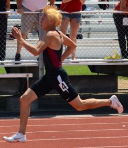 Athlete prepares for pole vault on a track with others watching.