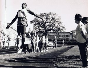 Athlete prepares for pole vault on a track with others watching.