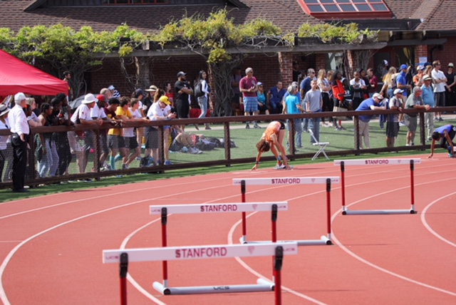 Athlete prepares for pole vault on a track with others watching.