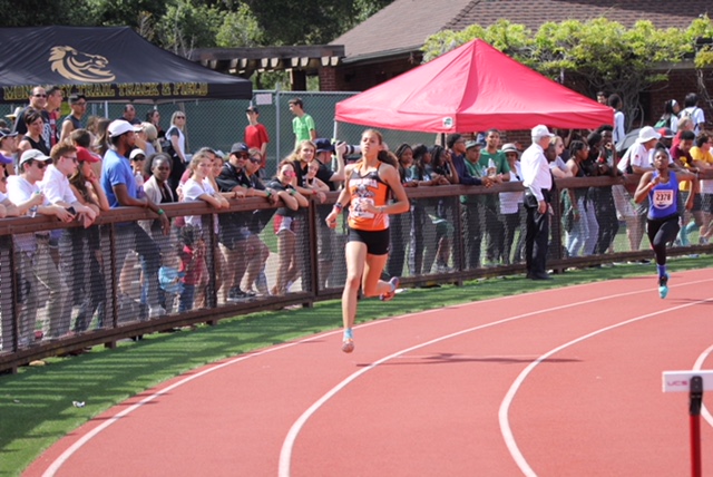 Athlete prepares for pole vault on a track with others watching.
