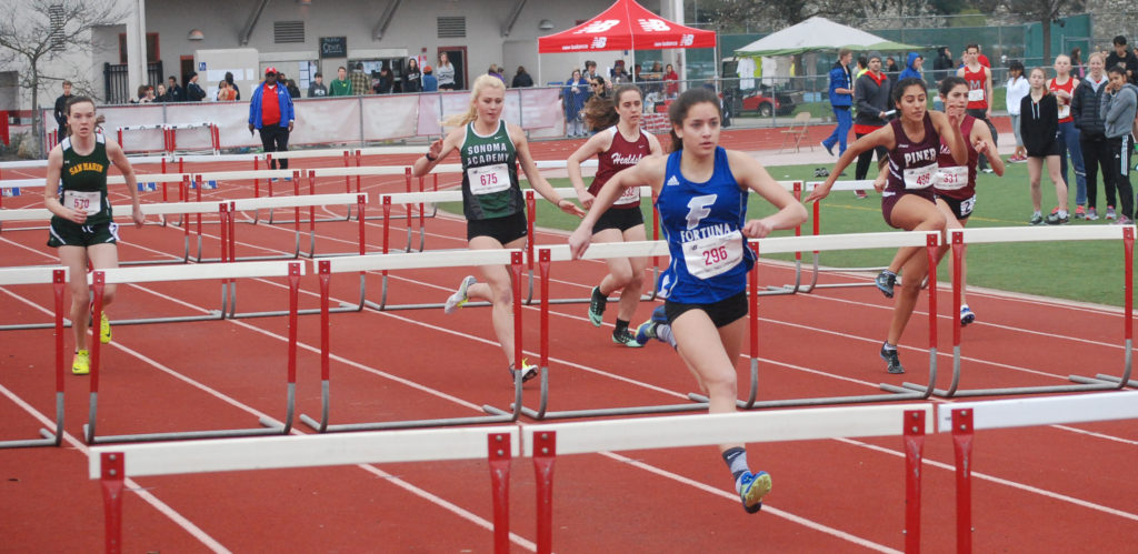 Athlete prepares for pole vault on a track with others watching.