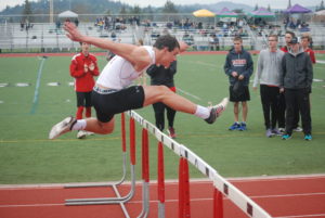 Athlete prepares for pole vault on a track with others watching.