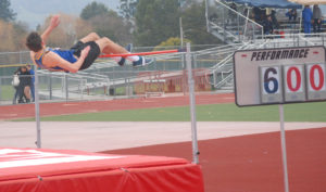 Athlete prepares for pole vault on a track with others watching.