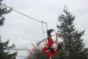 Athlete prepares for pole vault on a track with others watching.