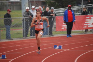 Athlete prepares for pole vault on a track with others watching.