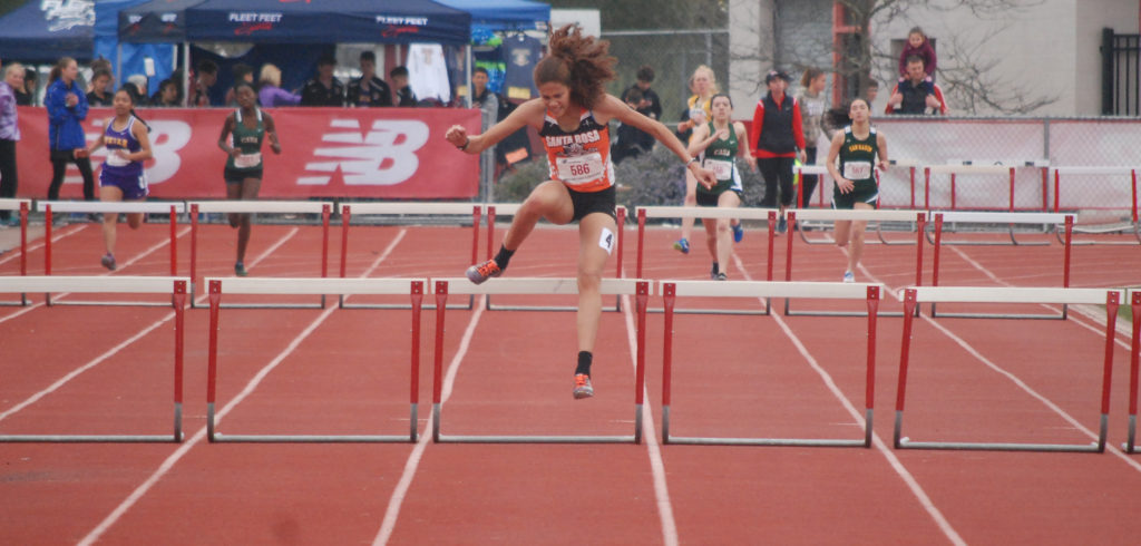 Athlete prepares for pole vault on a track with others watching.