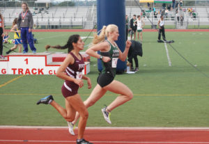 Athlete prepares for pole vault on a track with others watching.