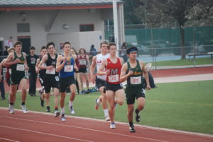 Athlete prepares for pole vault on a track with others watching.