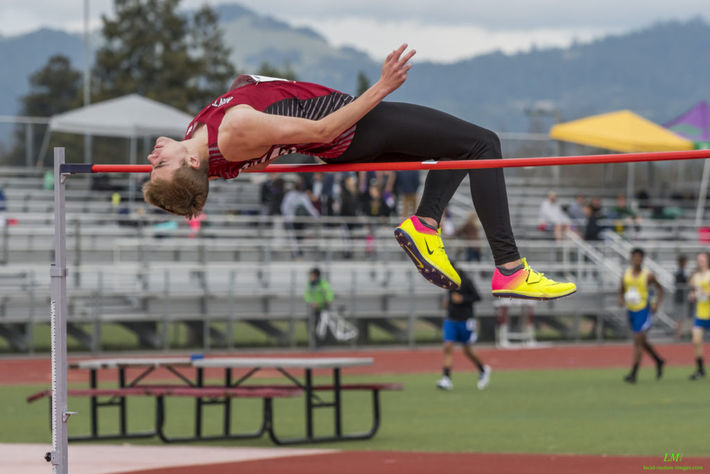 Athlete prepares for pole vault on a track with others watching.