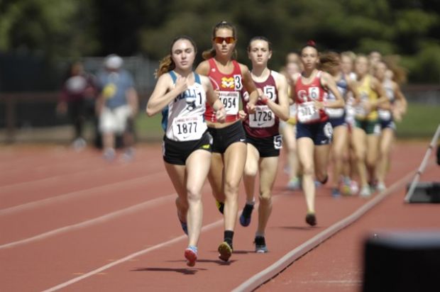 Athlete prepares for pole vault on a track with others watching.